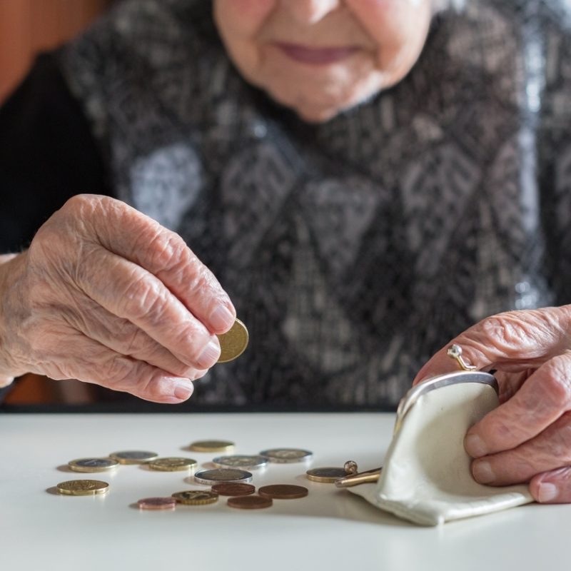 elderly woman sitting at the table counting money in her wallet.